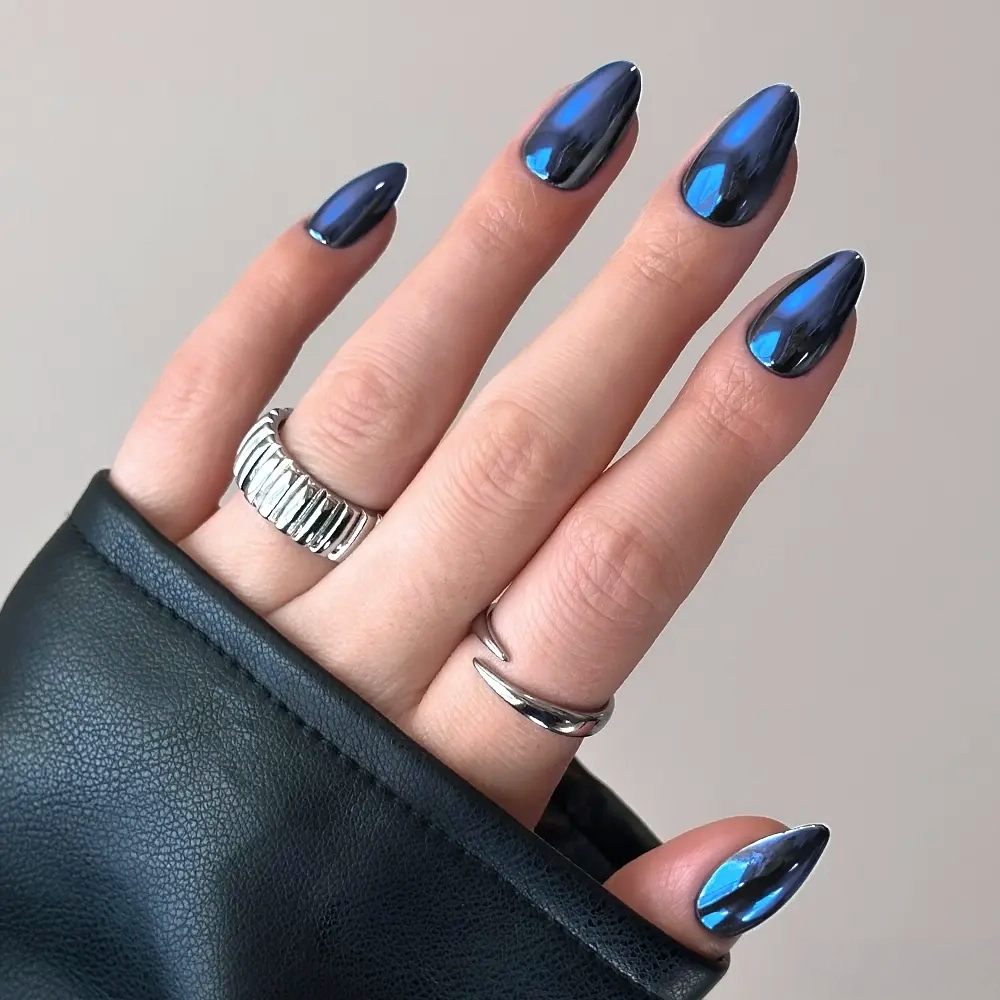 Blue Steel - Hand with short almond nails in Blue Steel metallic, reflective blue chrome, wearing two silver rings.