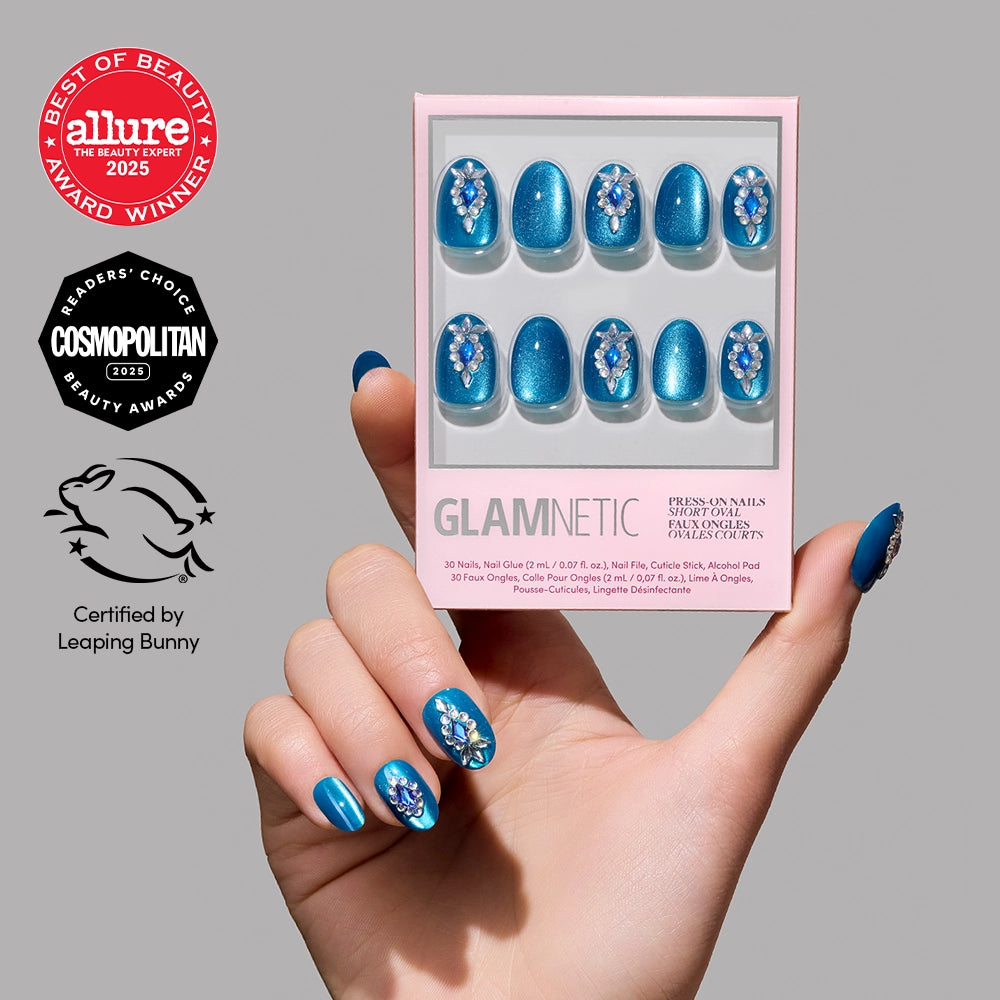 A hand with blue, floral-embellished Blue Topaz Press-On Nails holds a glamnetic nail set box featuring similar gemstone nails. Beauty award badges and a Leaping Bunny cruelty-free logo appear on the left.