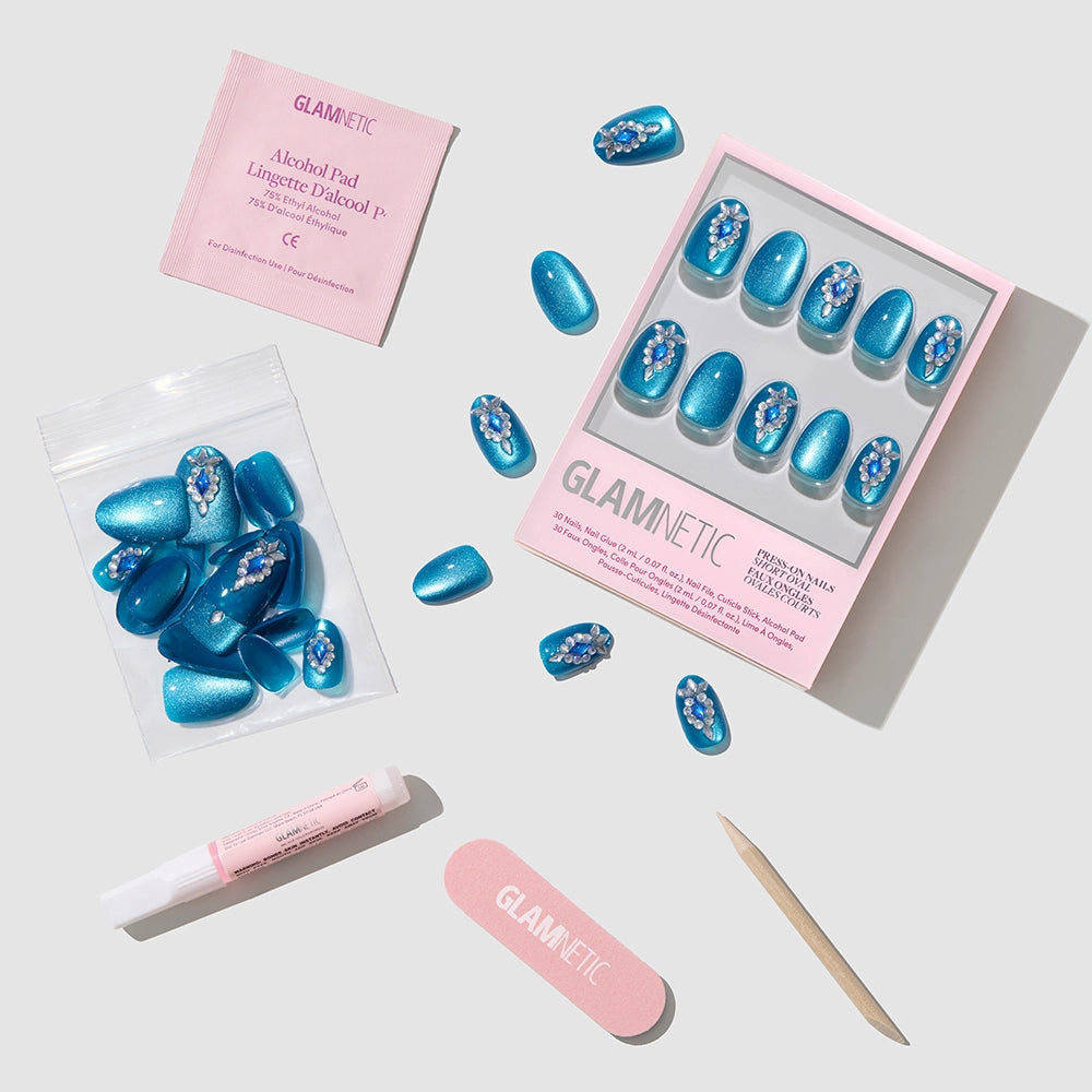 The glamnetic Blue Topaz set includes short oval press-on nails with flower designs, a pink nail file, wooden cuticle stick, nail glue, alcohol pad, and extra nails—displayed on a light gray background. - Product image