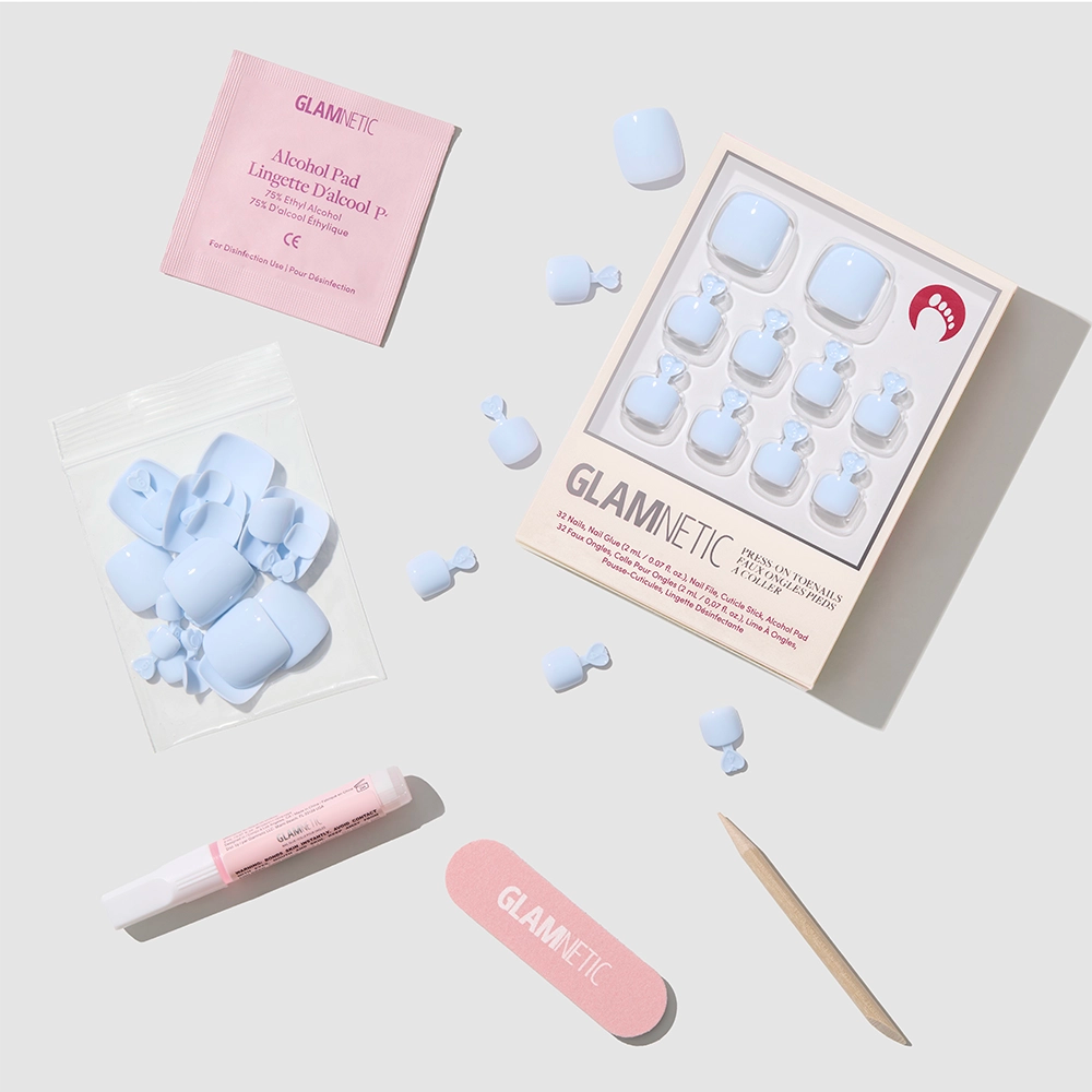 The glamnetic Blueberry Milk Toenail set includes glossy press-on toenails, a pink nail file, wooden cuticle stick, pink nail glue, alcohol pad, and extra nails, all arranged neatly against a white background. - Product image