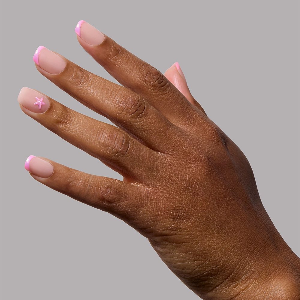 A hand wears glamnetic’s Blush Dunes press-on nails, featuring soft pink chrome tips and a white star accent, shown against a plain gray background. - Product image