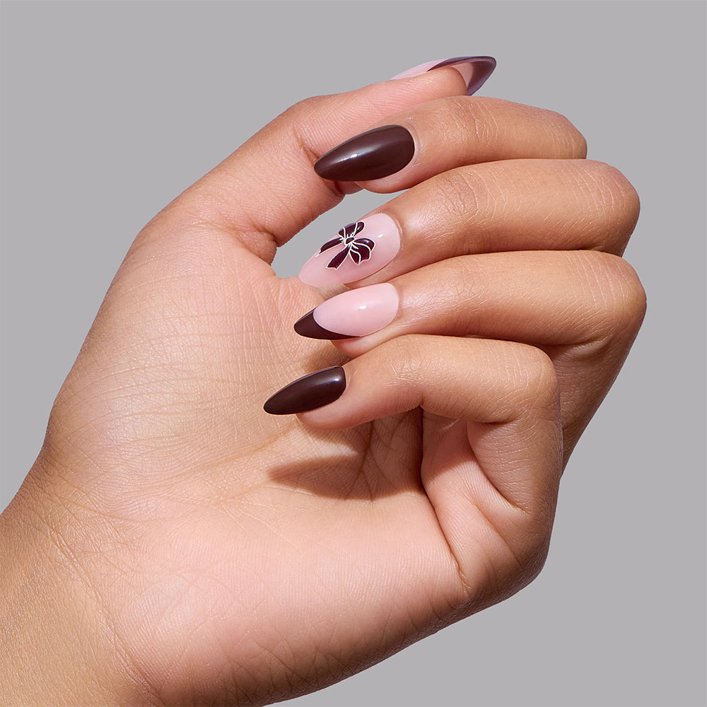 Glamnetic Bow Season short almond nails featuring an alternating design of solid dark brown and light pink with dark brown French tips and a small dark bow on one finger. - Product image