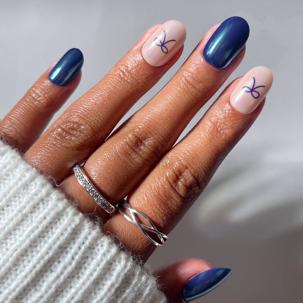 Glamnetic Bows & Bits short round press-on nails in alternating glossy dark blue and sheer nude with small blue bow accents.