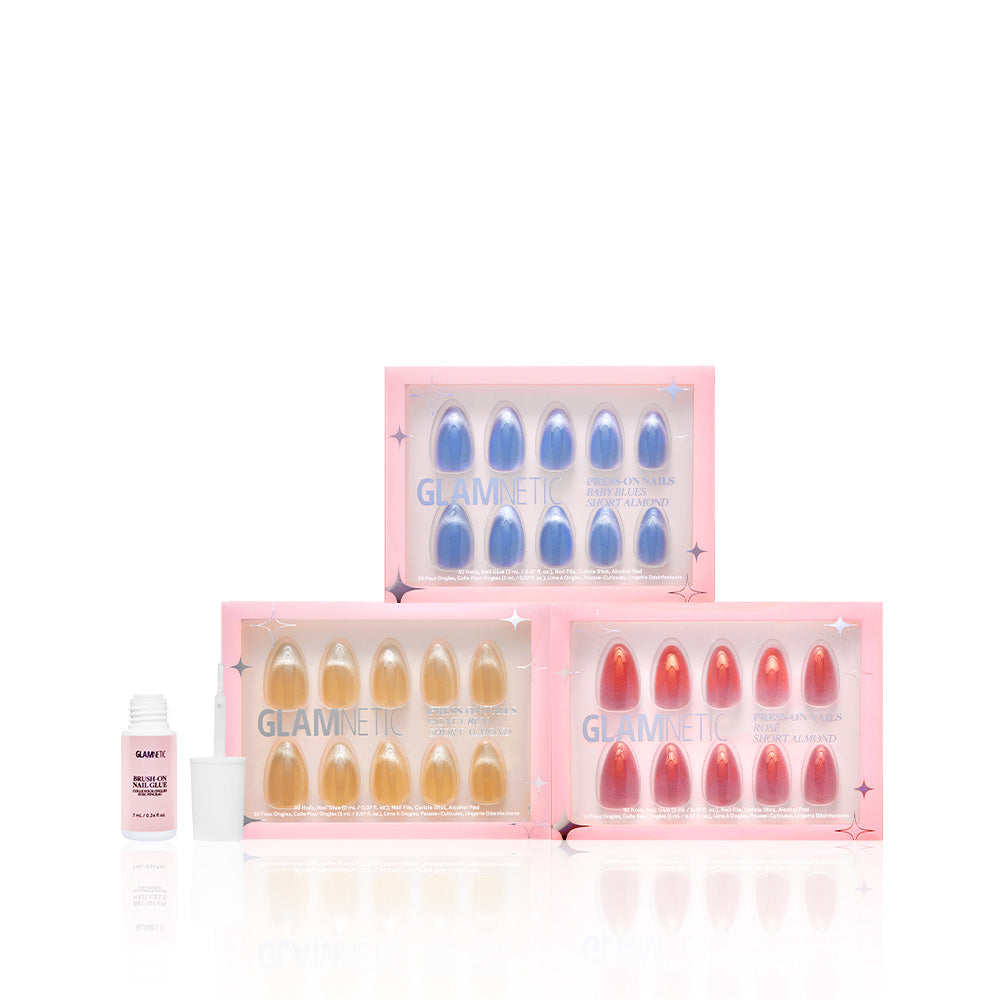 Three boxes of Glamnetic Velvet Haze press-on nails in blue, gold, and pink with a short almond shape and dimensional velvet finish are displayed on a white background next to an open bottle of nail glue. - Product image
