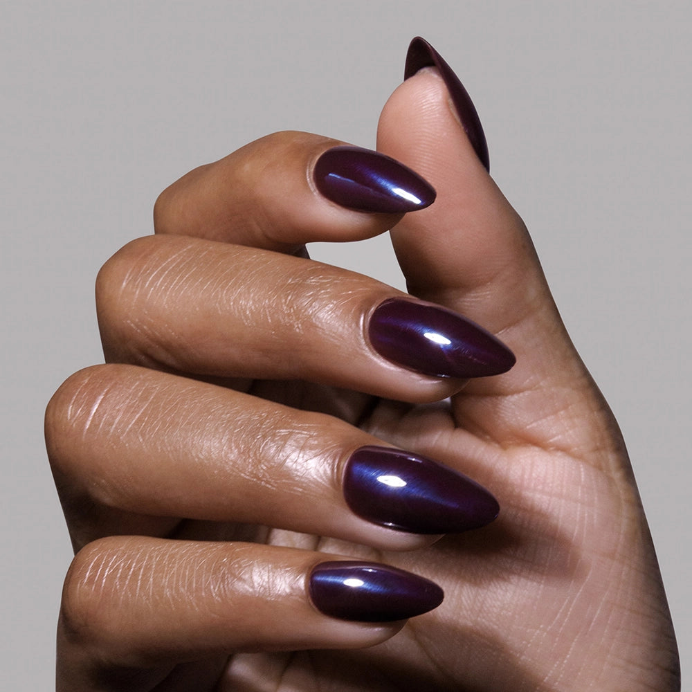A medium brown hand displays long, pointed nails coated in glamnetic’s Burgundy Chrome polish, giving a glossy, dark purple finish for a chic and modern look. - Product image