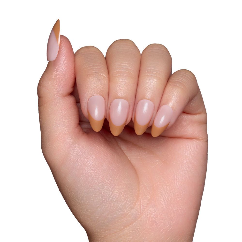 A hand with glamnetic Café Crème almond-shaped, reusable nails—nude base and brown French tips—is displayed against a white background for a cozy vibe. - Product image