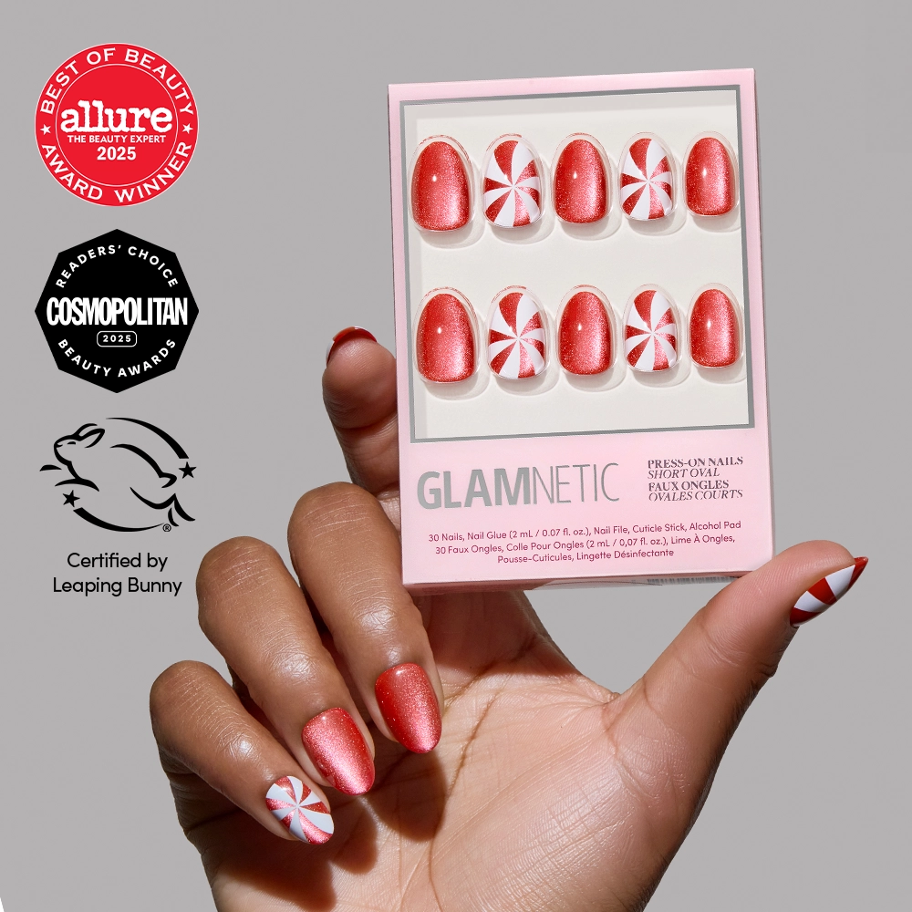A hand with red and white peppermint swirl nail art holds a glamnetic Candy Crush press-on nails set. Beauty award logos and a leaping bunny certification symbol are visible in the background, accentuating these festive short oval nails. - Product image