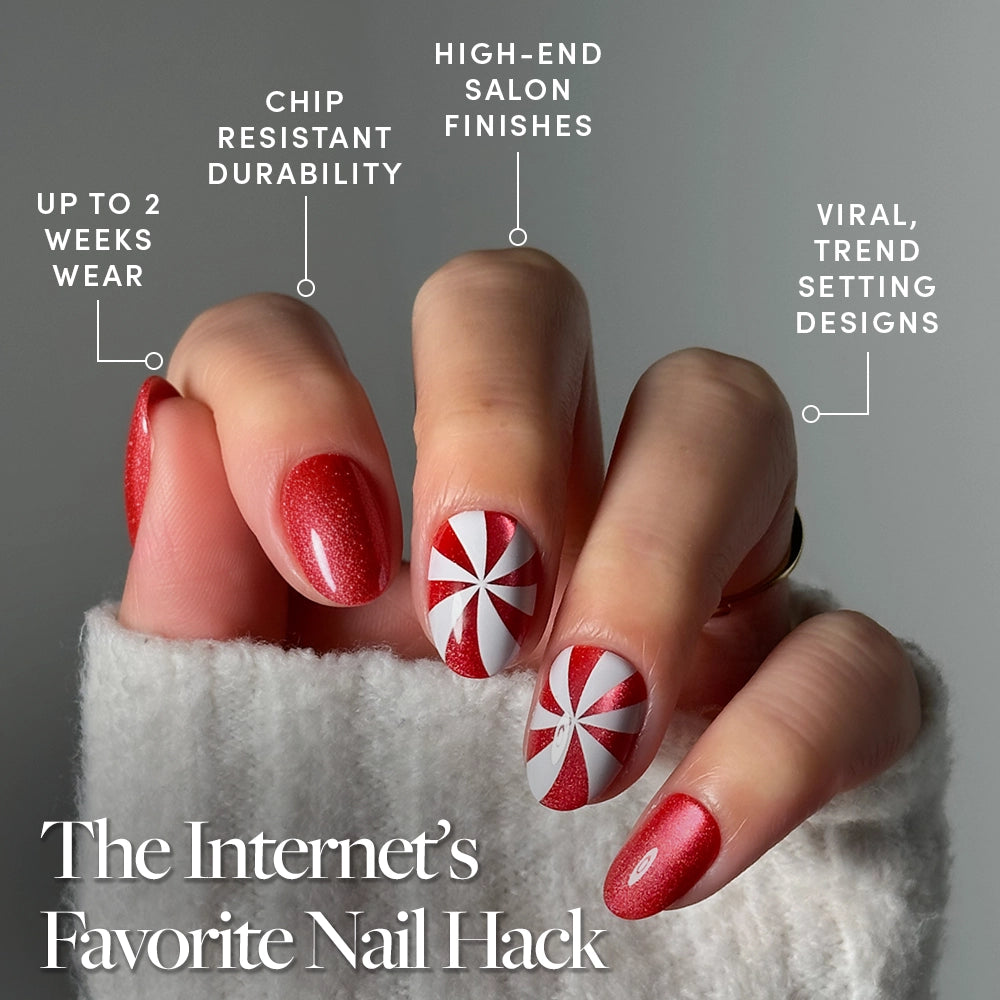 A hand with glossy red and white peppermint swirl nail art from the glamnetic Candy Crush set. These holiday press-on nails in a trendy short oval shape feature high-end finishes and viral designs, offering up to 2 weeks of chip-resistant wear. Sweater sleeves partially cover the fingers, highlighting this eye-catching look. - Product image