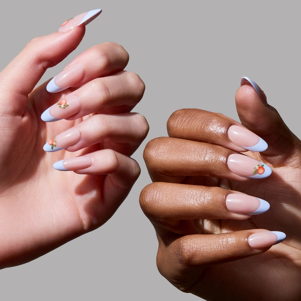Two hands with long, almond-shaped glamnetic Capri Coast press-on nails—pale pink base, light blue tips, and small peach art on the ring fingers—create a salon-quality look against a plain gray background. - Product image