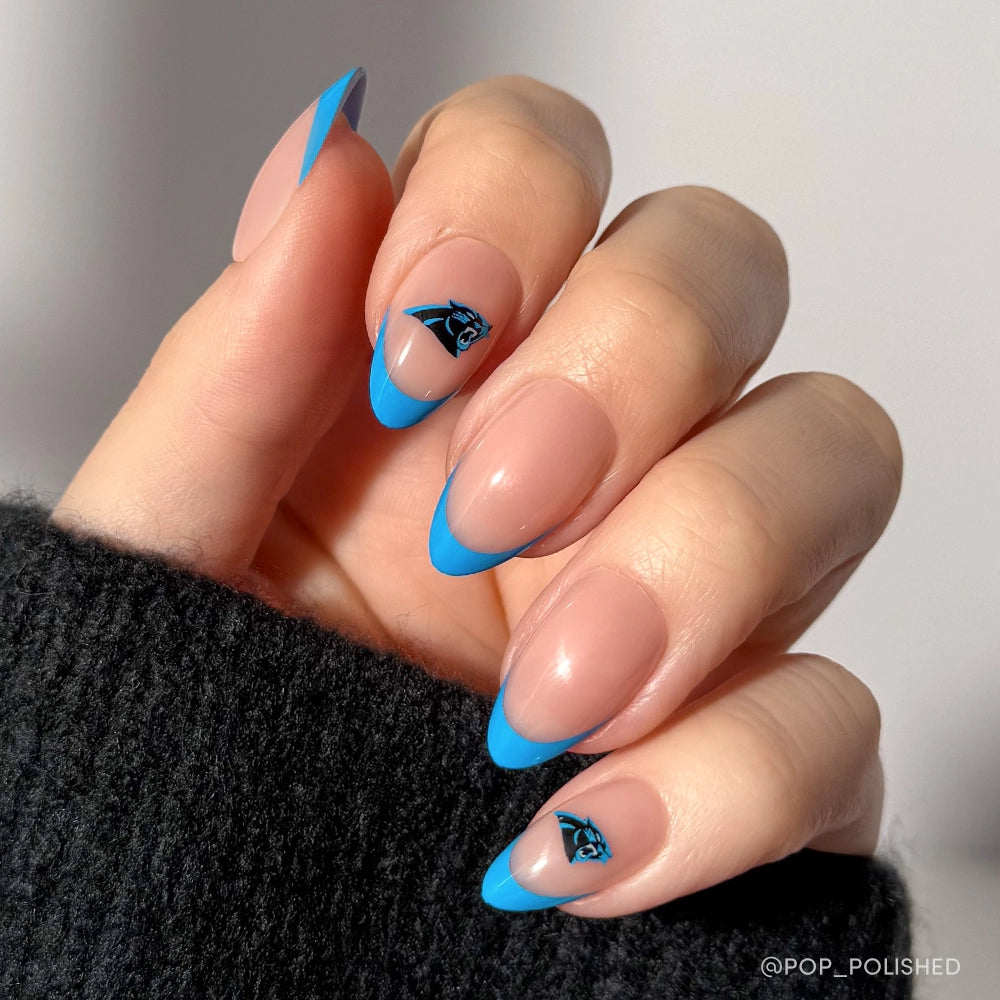 Show off your team spirit with the glamnetic Carolina Panthers Press-On Nail Set—almond-shaped press-ons with a nude base, bold blue French tips, and black Panthers logos on the ring and thumb, paired perfectly with a black sweater.