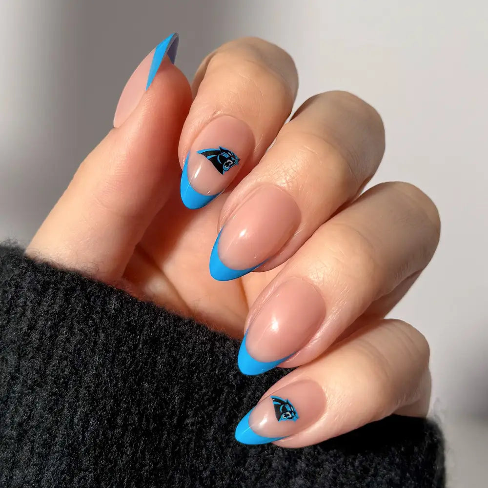 A hand wearing glamnetic NFL Press-On Nails, styled with almond-shaped blue French tips and a small black and blue panther logo accent on two nails, shown against a soft neutral background. - Product image