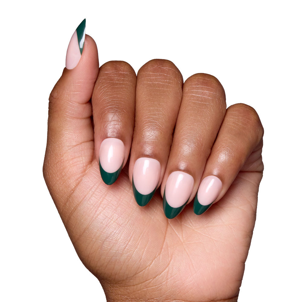 A hand with short almond nails featuring a nude base and dark green French tips, held against a white background, showcases the elegant Château set by glamnetic. - Product image
