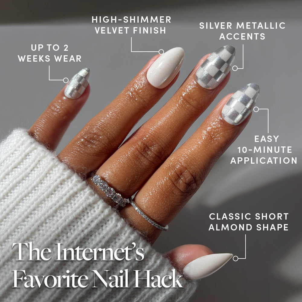 A hand with short almond Glamnetic Check-Mated nails featuring white and metallic silver checkered patterns, a high-shimmer velvet finish, silver metallic accents, easy application, and two-week wear. - Product image