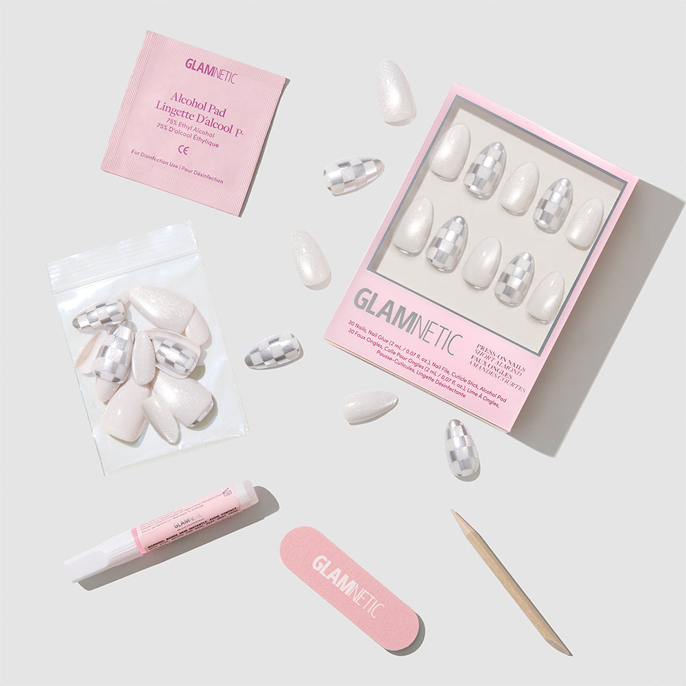 Glamnetic Check-Mated short almond press-on nail kit featuring a box of white and silver checkered nails, loose nails, nail glue, an alcohol pad, a nail file, and a wooden cuticle pusher. - Product image