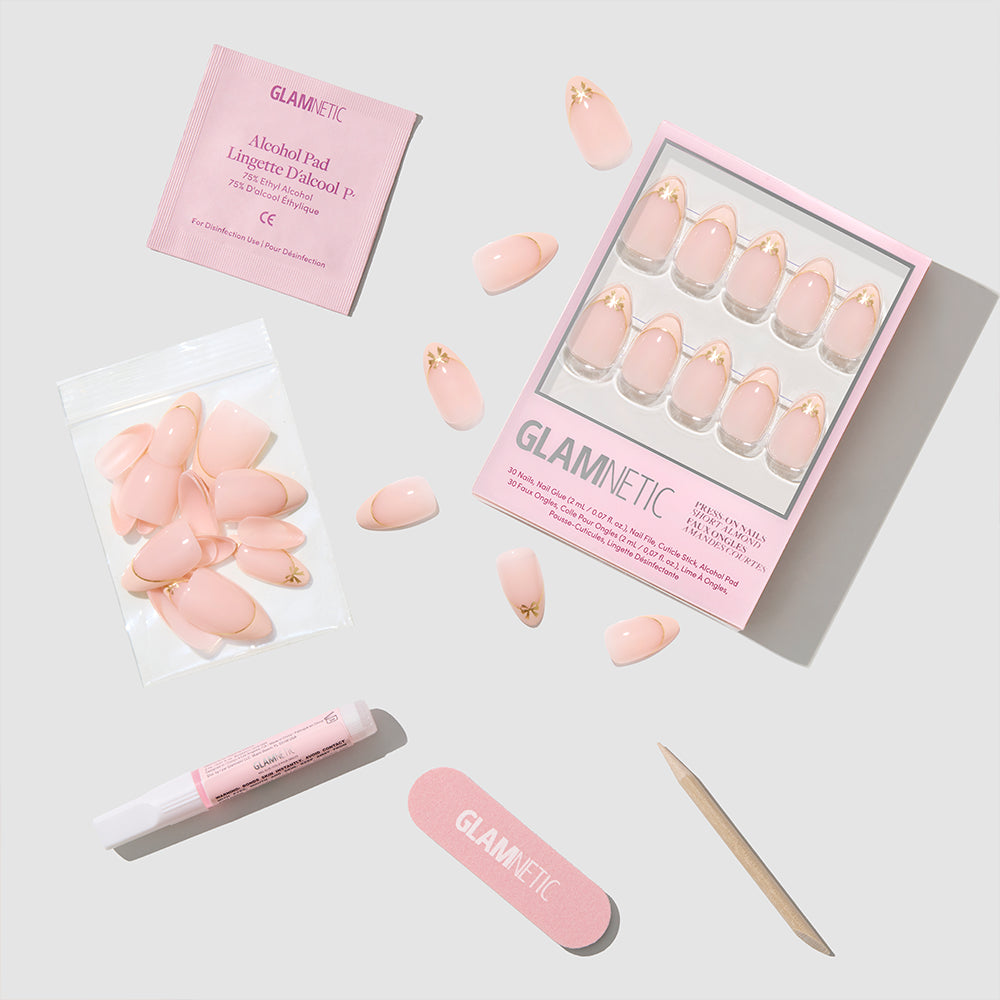 Glamnetic Cindy Lou short almond press-on nails featuring a nude base with gold heart accents, packaged with glue, a nail file, a cuticle stick, and an alcohol pad. - Product image