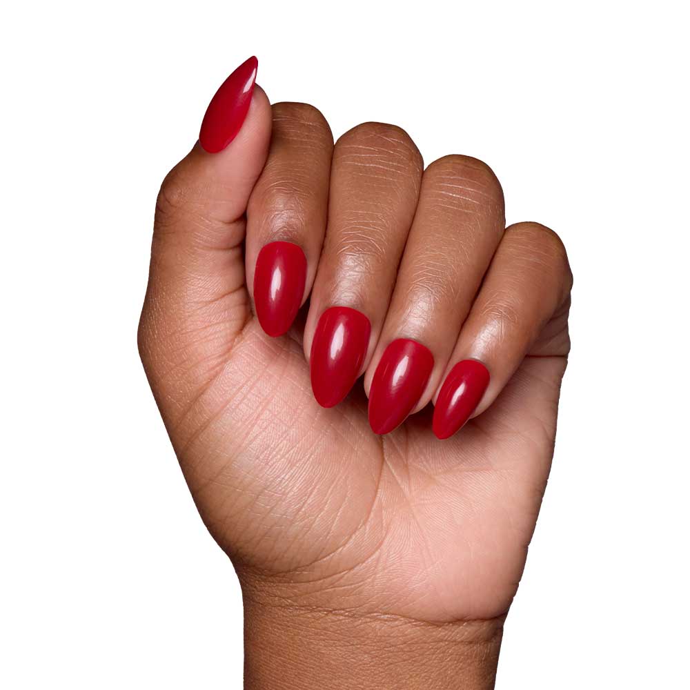 A hand with medium brown skin tone displays the glamnetic Classic Red glossy almond-shaped nails, fingers slightly curled, set against a white background. - Product image