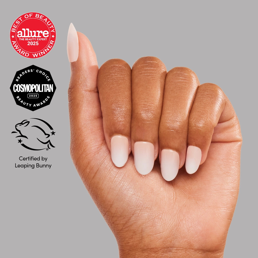 A hand with neatly manicured, pale pink "Creamer" vegan nails by glamnetic is shown against a gray background. Beauty award logos and a cruelty-free Leaping Bunny certification logo appear on the left side. - Product image