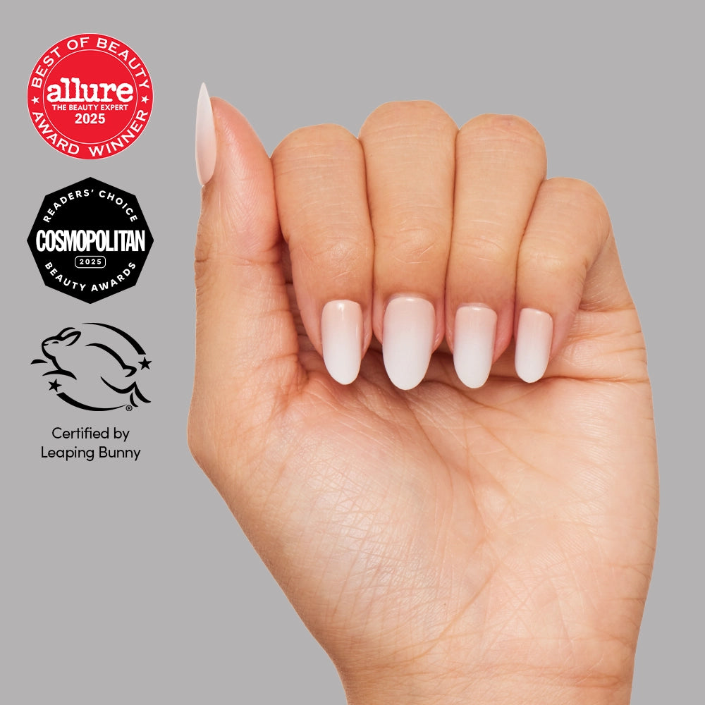 A hand with almond-shaped glamnetic Creamer vegan nails in a light pink ombre is shown against a gray background, featuring award badges from Allure and Cosmopolitan plus Leaping Bunny certification. - Product image