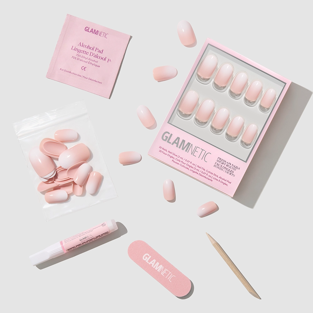The glamnetic Creamer set includes pink french tip press-on nails, an alcohol pad, nail glue, a nail file, a wooden cuticle stick, and extra nails neatly arranged on a light gray background. - Product image