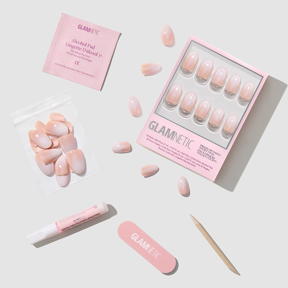 The glamnetic Crystal Glaze kit features short oval nude-to-white ombré press-on nails, an alcohol pad, pink nail file, cuticle stick, nail glue, and extra nails—all displayed neatly on a light background. - Product image