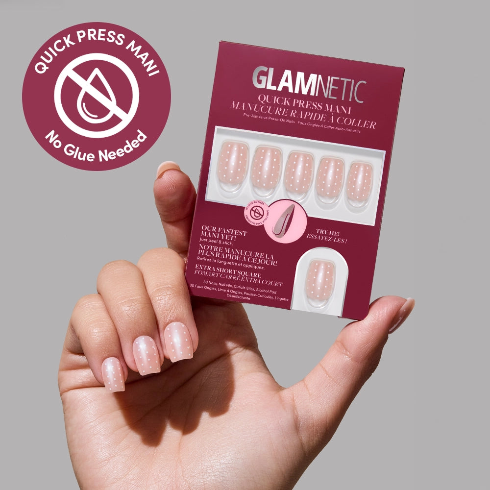 A hand with neatly applied pink and white polka dot Dainty Dots no-glue press-on nails holds a glamnetic kit. A badge reads “Quick Press Mani, No Glue Needed” on a light gray background.