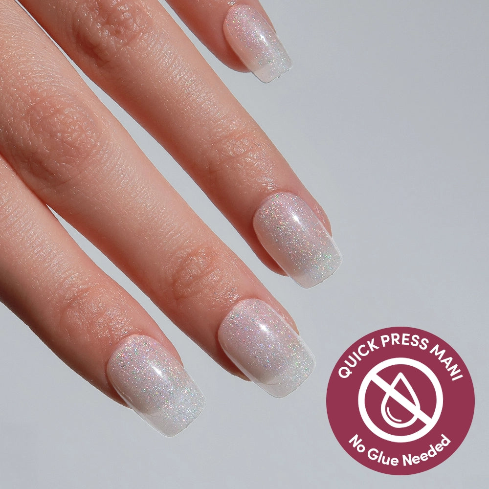 A hand with square, short, iridescent white press-on nails from the Daydream Veil set by glamnetic. A circular badge reads QUICK PRESS MANI, No Glue Needed.