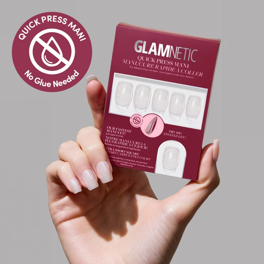A hand with light pink, shimmery Daydream Veil press-on nails by glamnetic holds the box. A circular badge says “Quick Press Mani, No Glue Needed” with a crossed-out glue bottle icon on the left.
