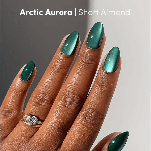 Short almond nails in metallic green (Arctic Aurora by glamnetic). A silver ring with three stones highlights the bold emerald shade. Text: Arctic Aurora | Short Almond.