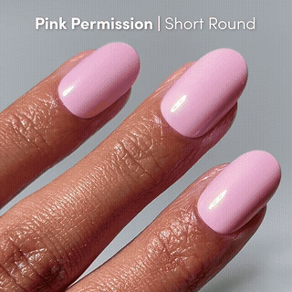 A hand with short squoval nails painted a glossy pastel pink shade, labeled Pink Control by glamnetic, is shown against a light gray background—ideal for fans of glossy blush nails.