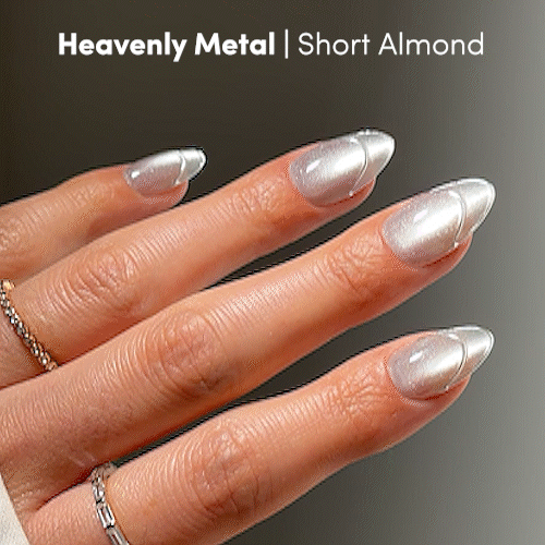 A hand with short, almond-shaped nails from glamnetic’s Heavenly Metal collection showcases a striking metallic silver finish. The sleek, shimmering nails are paired beautifully with thin gold rings for an eye-catching look. - Product image