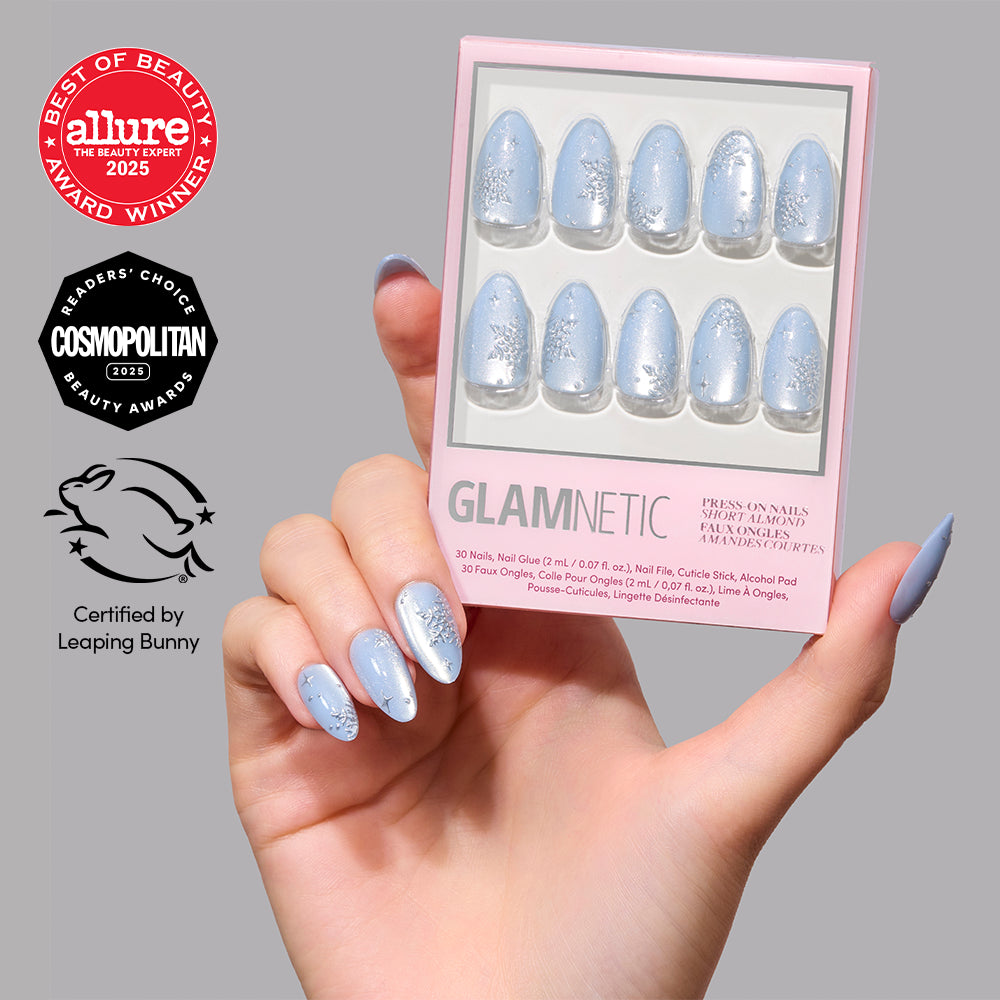 A hand holds a box of Glamnetic December Sky light blue velvet-effect short almond press-on nails decorated with silver snowflake designs. - Product image