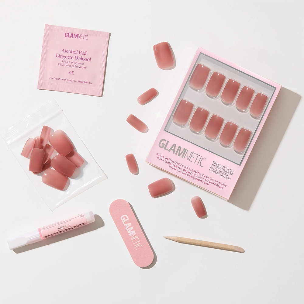 The glamnetic Dusty Pink press-on nails feature a medium square shape and glossy finish, with application tools—nail file, cuticle stick, glue tube, alcohol pad, and extra nails—arranged neatly on a white surface. - Product image