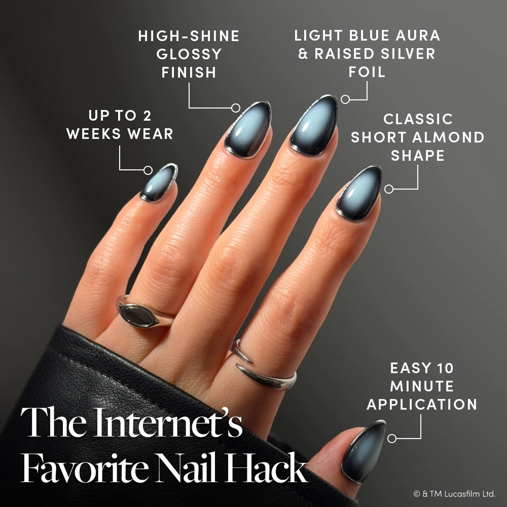 A hand adorned with glossy, short almond-shaped blue nails featuring a foil effect highlights the stunning STAR WARS™ press-on nails, “Emperor,” by glamnetic. Text emphasizes a quick 10-minute application, long-lasting wear for up to 2 weeks, and an ultra high-shine finish. The look is completed with silver rings and a black sleeve. - Product image