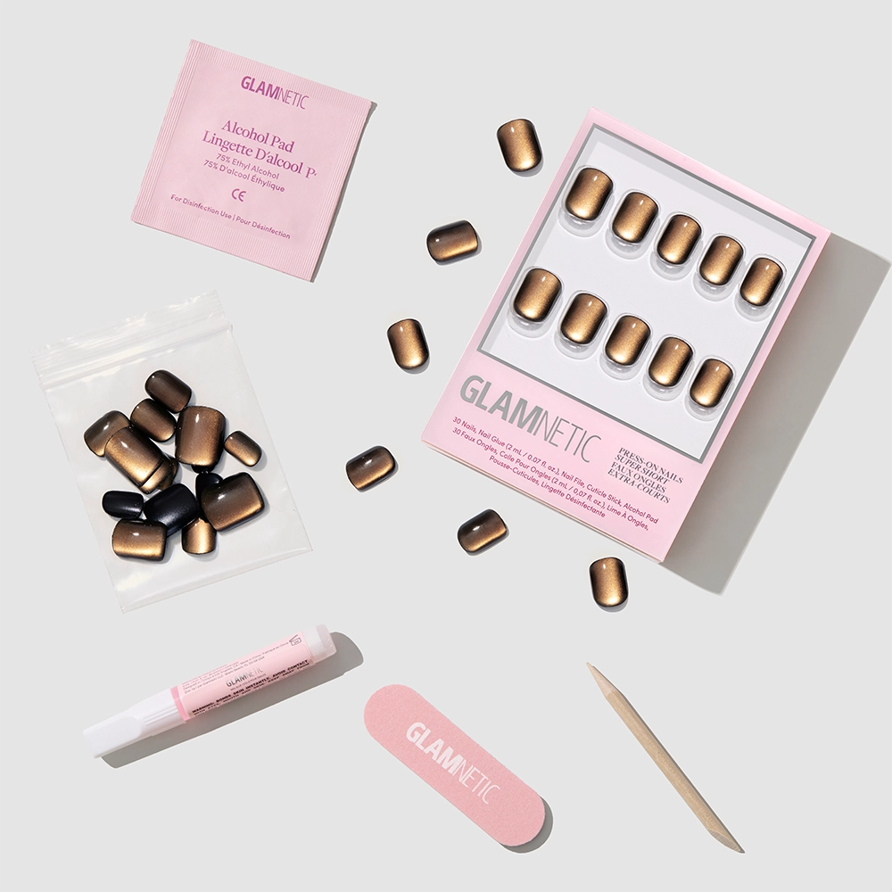 Enstatite Press-On Nails by glamnetic, including a pink box, alcohol pad, nail glue, mini file, cuticle stick, and extra nails, displayed on a light gray surface. - Product image