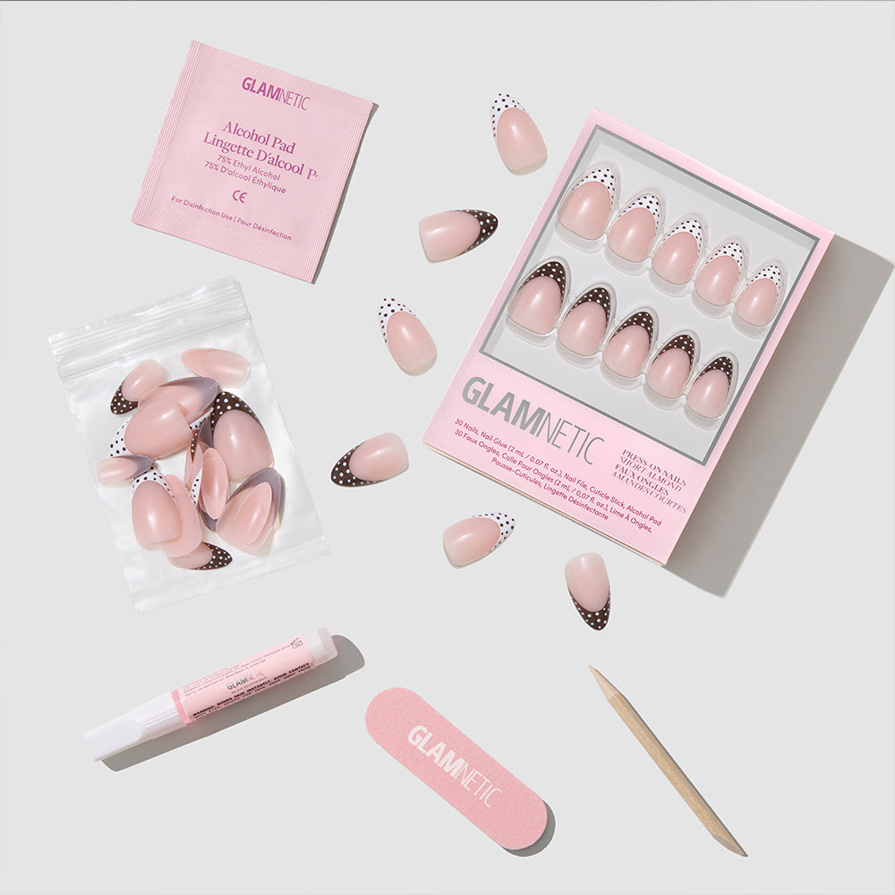 Polka In Positano by glamnetic is a cruelty-free press-on nail set featuring short almond-shaped pink nails with black and white tips, plus glue, alcohol pad, nail file, cuticle stick, and extra nails—all shown on a light background. - Product image
