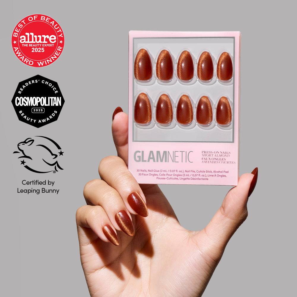 A hand with shimmering brown short almond press-on nails (Sicilian Sun by glamnetic) holds a pink GLAMNETIC box. Allure, Cosmopolitan, and Leaping Bunny certification logos are shown beside the hand.