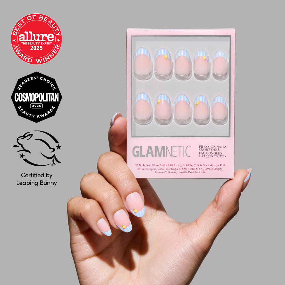 A hand with glossy pink short oval nails with blue and gold tips holds a box of glamnetic Summer Fresco press-on nails. Award badges from Allure, Cosmopolitan, and Leaping Bunny certification appear on the left.