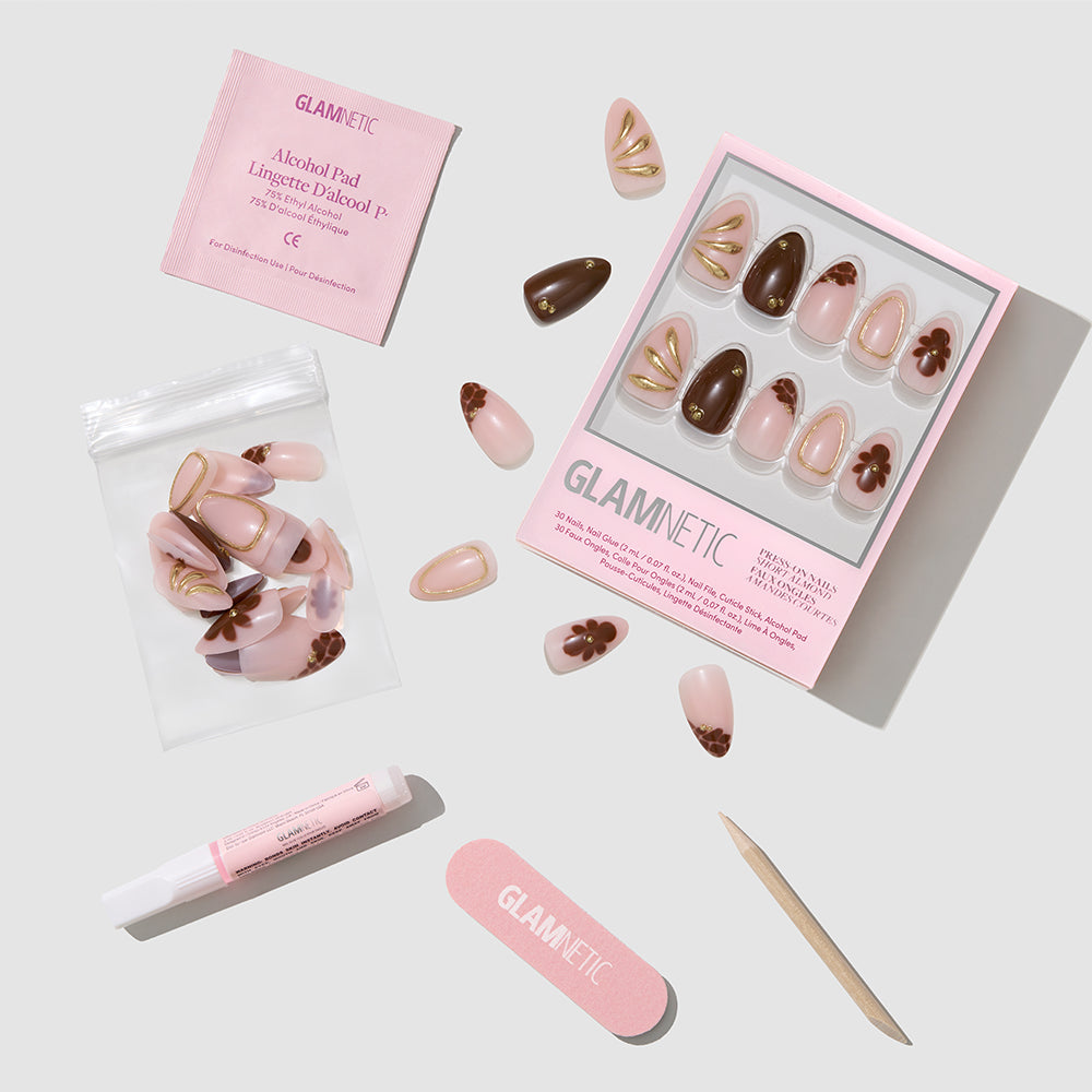 The Sunbaked short almond press-on nails by glamnetic feature pink, brown, and gold designs. The set includes glue, a file, cuticle stick, extra nails in a zip bag, and an alcohol pad—arranged on a light background. - Product image