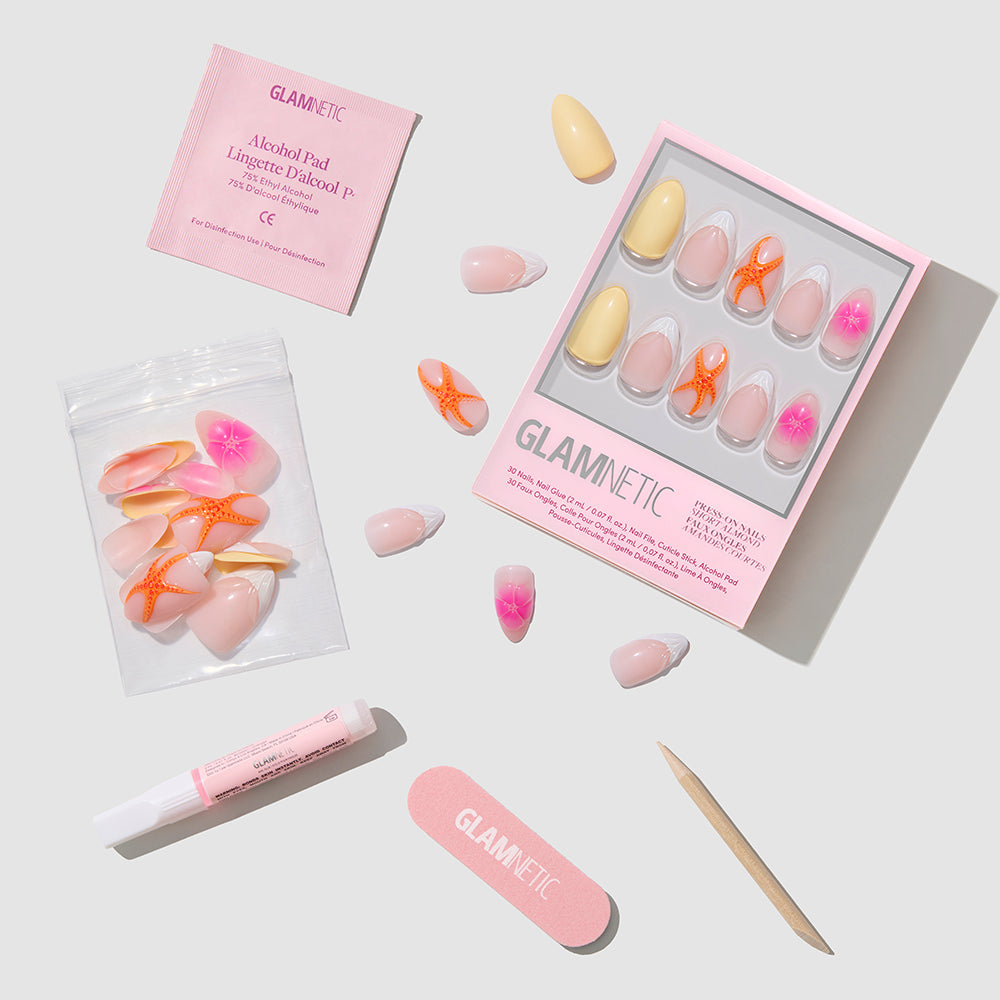 A flat lay of glamnetic Sunset Tide short almond press-on nails features a box with assorted pink and orange French tip designs, nail glue, file, cuticle stick, alcohol pad, and extra nails arranged on a light gray background. - Product image
