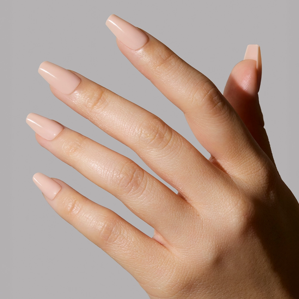 A hand with medium-length, square nails painted in glamnetics Exposed, a pinky nude shade with a glossy, high-shine finish, is shown against a plain light gray background. - Product image