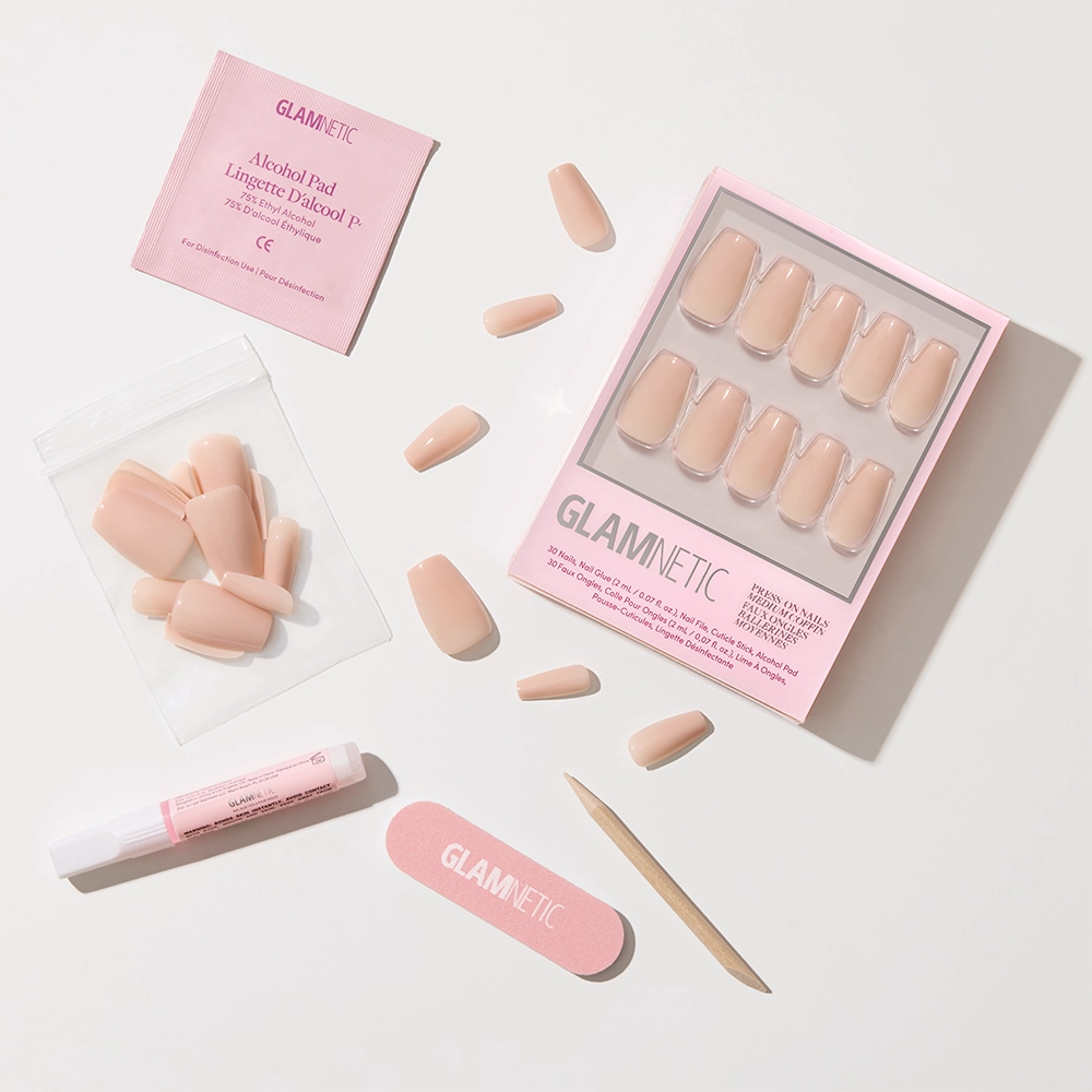 Exposed by glamnetic: a pinky nude, coffin-shaped press-on nail set with a high-shine finish, packed in a pink Glamnetic box with glue, alcohol pad, nail file, cuticle stick, and extra nails, all arranged on a white background. - Product image