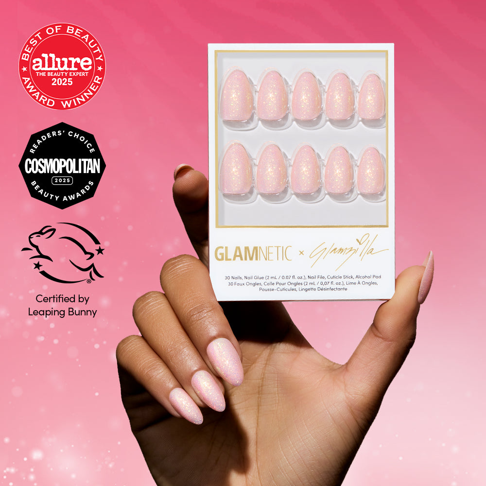 A hand with light pink, holographic shimmer nails holds a box of glamnetic FAIRY FLEXX press-ons against a pink background, with Allure, Cosmopolitan, and Leaping Bunny badges highlighting their vegan, cruelty-free formula.