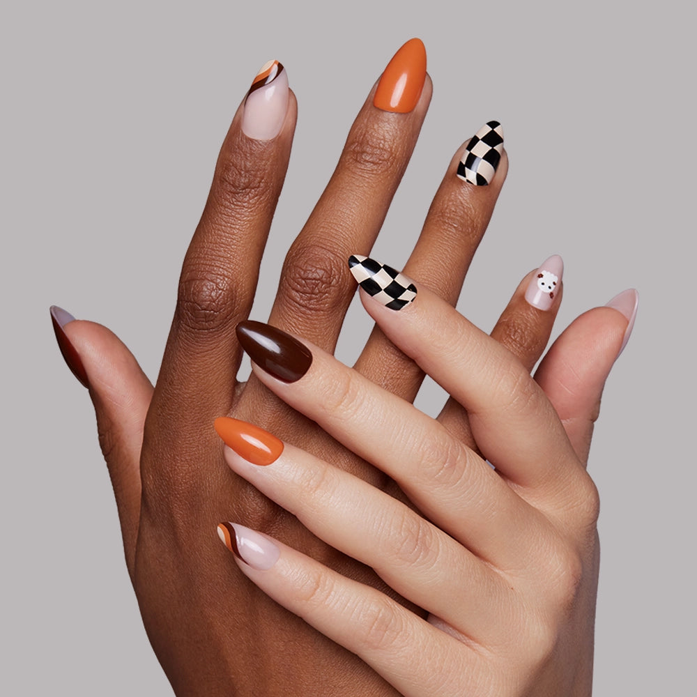 Two hands with short almond-shaped nails show off glamnetics Fall Boo Nail Set—featuring orange, brown, nude, black and white checkerboard designs, plus a cute white ghost—against a plain gray background. - Product image