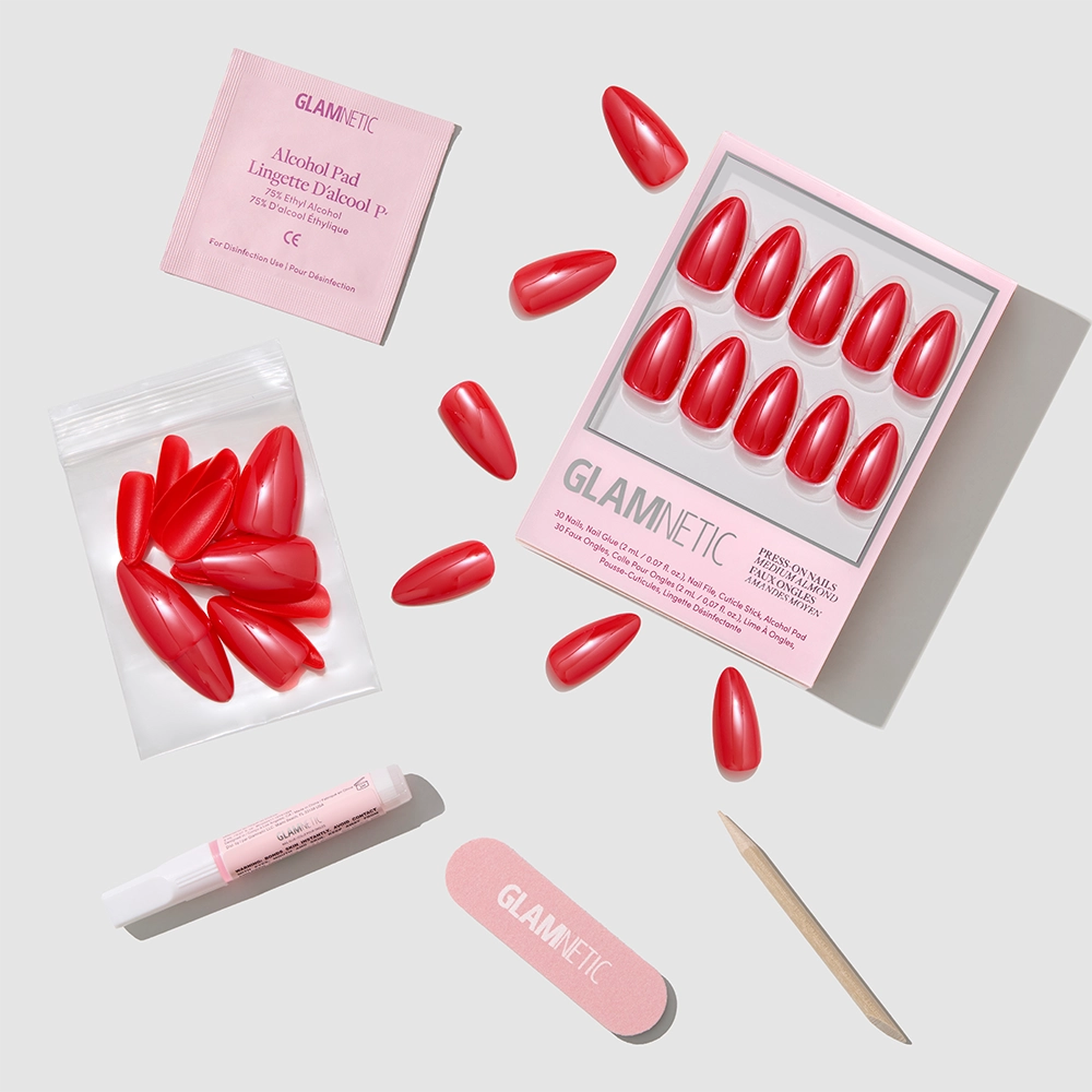 The Fearless Red press-on nails by glamnetic come with accessories—alcohol pad, nail glue, file, cuticle stick, and extra nails—offering a salon-quality manicure, all displayed on a light gray background.
