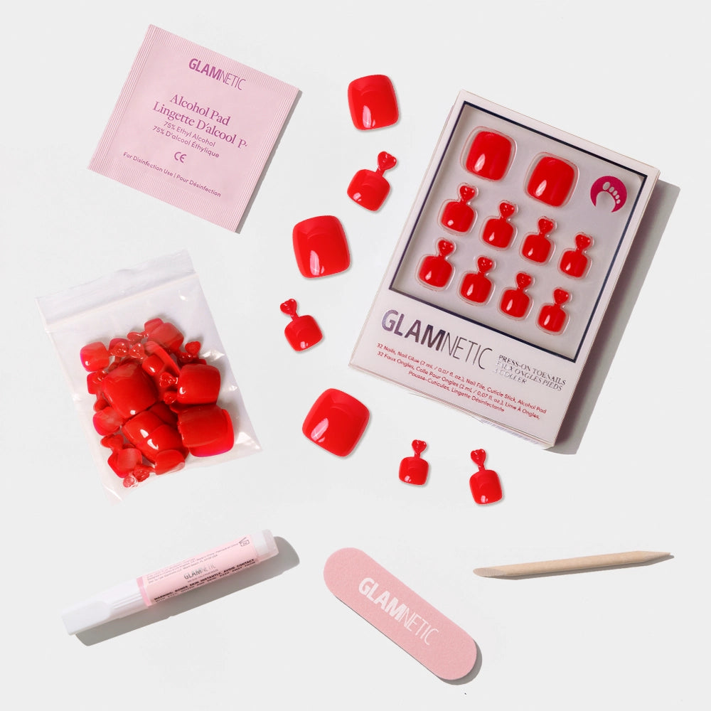 A flat-lay of the Glamnetic bold red press-on toenail kit with full contents laid out, including glue and nail care tools. - Product image