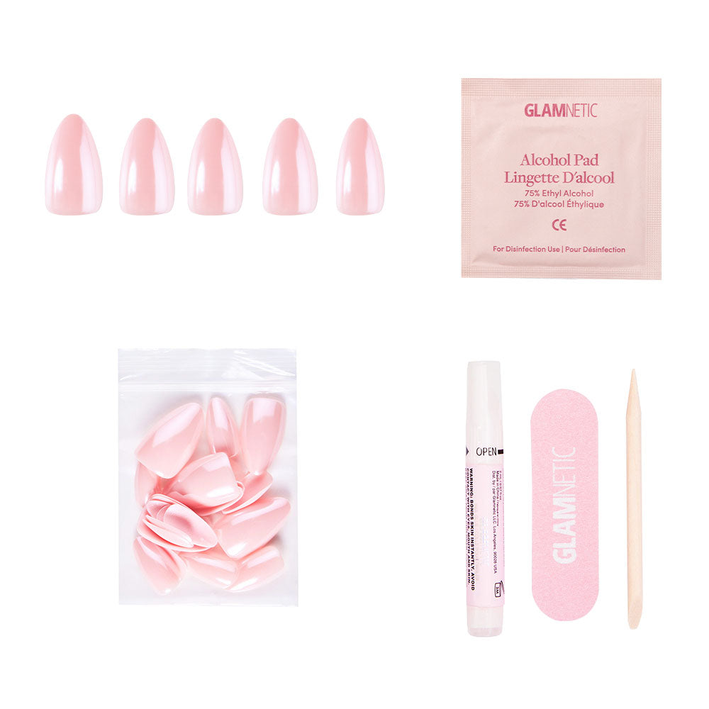The First Kiss nail set by glamnetic includes blush pink nails, extra nails, nail glue, a pink file, a wooden cuticle stick, and an alcohol pad—all neatly displayed on a white background. - Product image