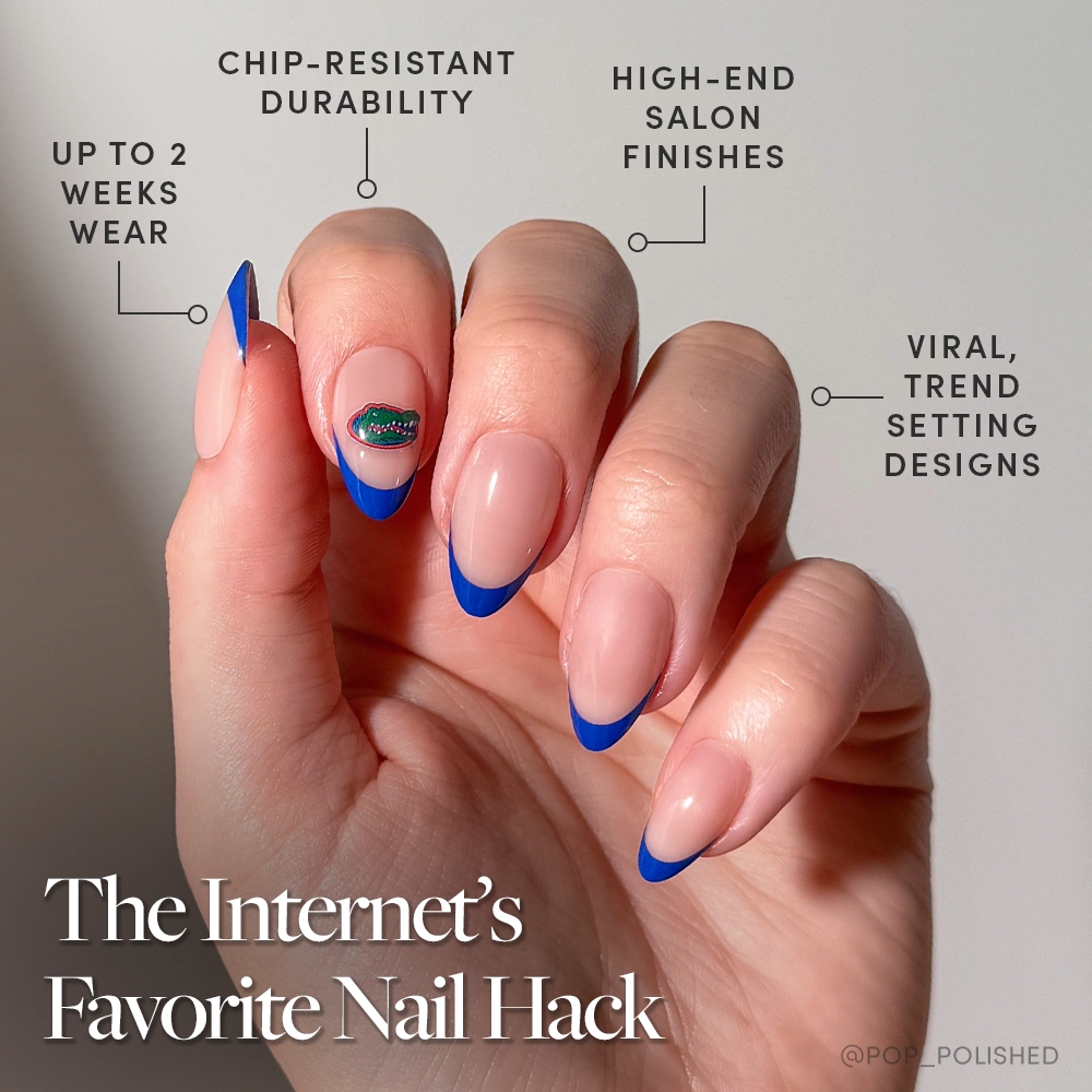 A hand with long, almond-shaped nude nails features bold blue French tips and an alligator sticker—showcasing the glamnetic Florida Gators Press-On Nail Set for a durable, salon-quality manicure inspired by trending styles. - Product image