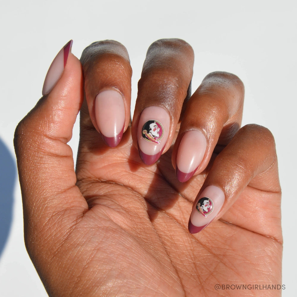 Showcased on a white background, the glamnetic Florida State Seminoles Press-On Nail Set features almond-shaped, nude nails with garnet red French tips and two accent nails sporting the team logo near the cuticle for a salon-quality finish.