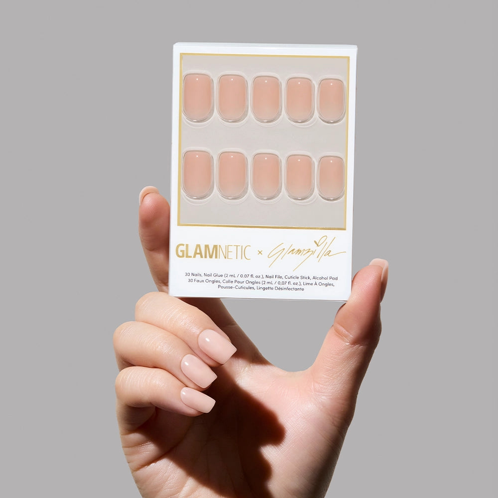 Hand holding a package of Glamnetic press-on nails against a gray background