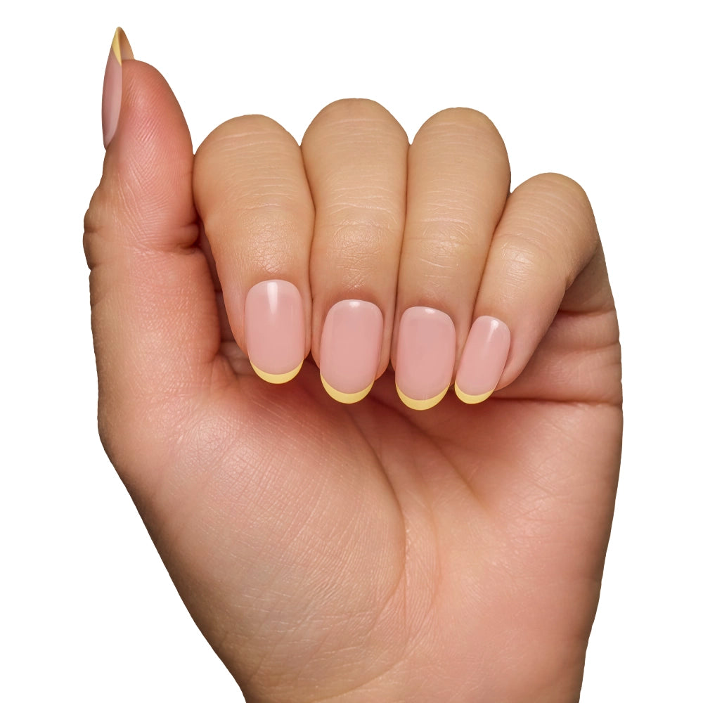 A hand with fingers curled inward displays salon-quality durability and neatly manicured nails from the glamnetic French Butter set, featuring a nude base and pastel yellow French tips against a white background. - Product image